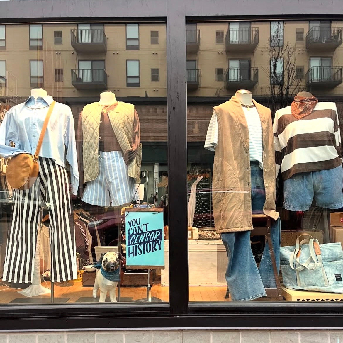 Display of sustainable women's clothing and accessories in a store window with a sign.