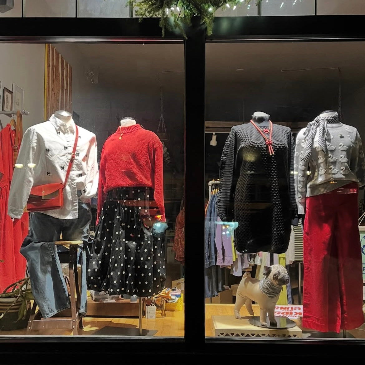 Display of sustainable women's clothing and accessories in a store window with mannequins and a small dog figure.