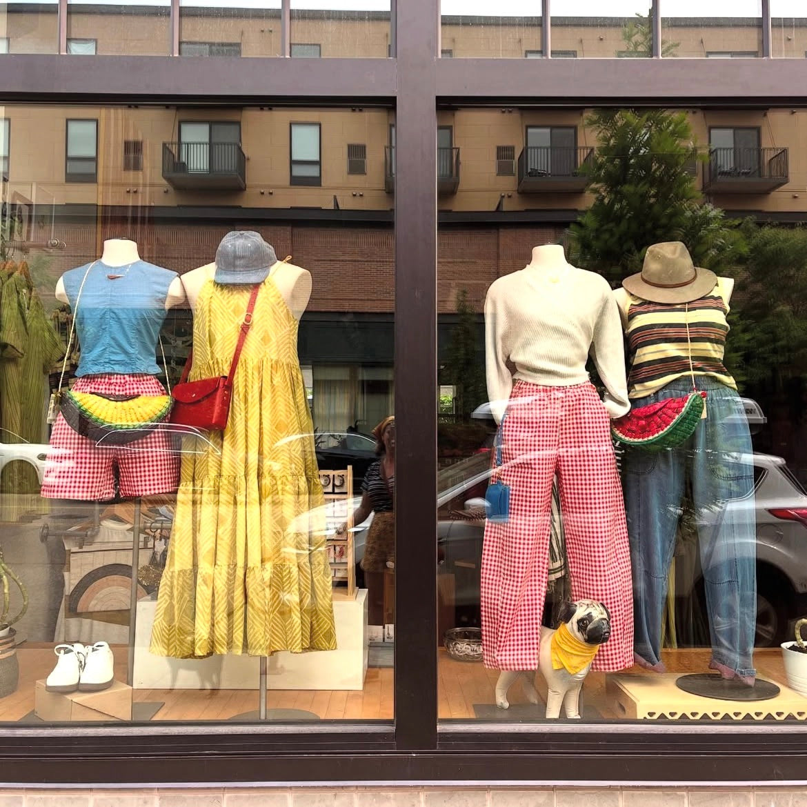 Mannequins in a store window display with sustainable women's clothing and accessories, including a dog.