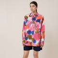 A model wearing an oversized multicolored shirt with a classic collar and long sleeves, paired with dark shorts and black shoes.