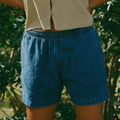 Person wearing a beige top and blue shorts in a natural setting.