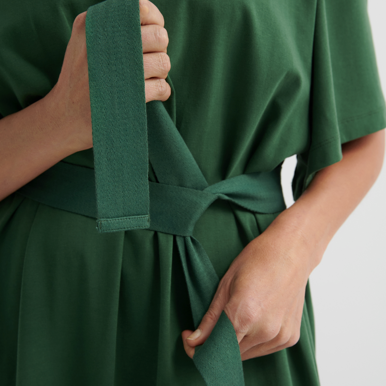 Green dress with a belt being adjusted against a neutral background