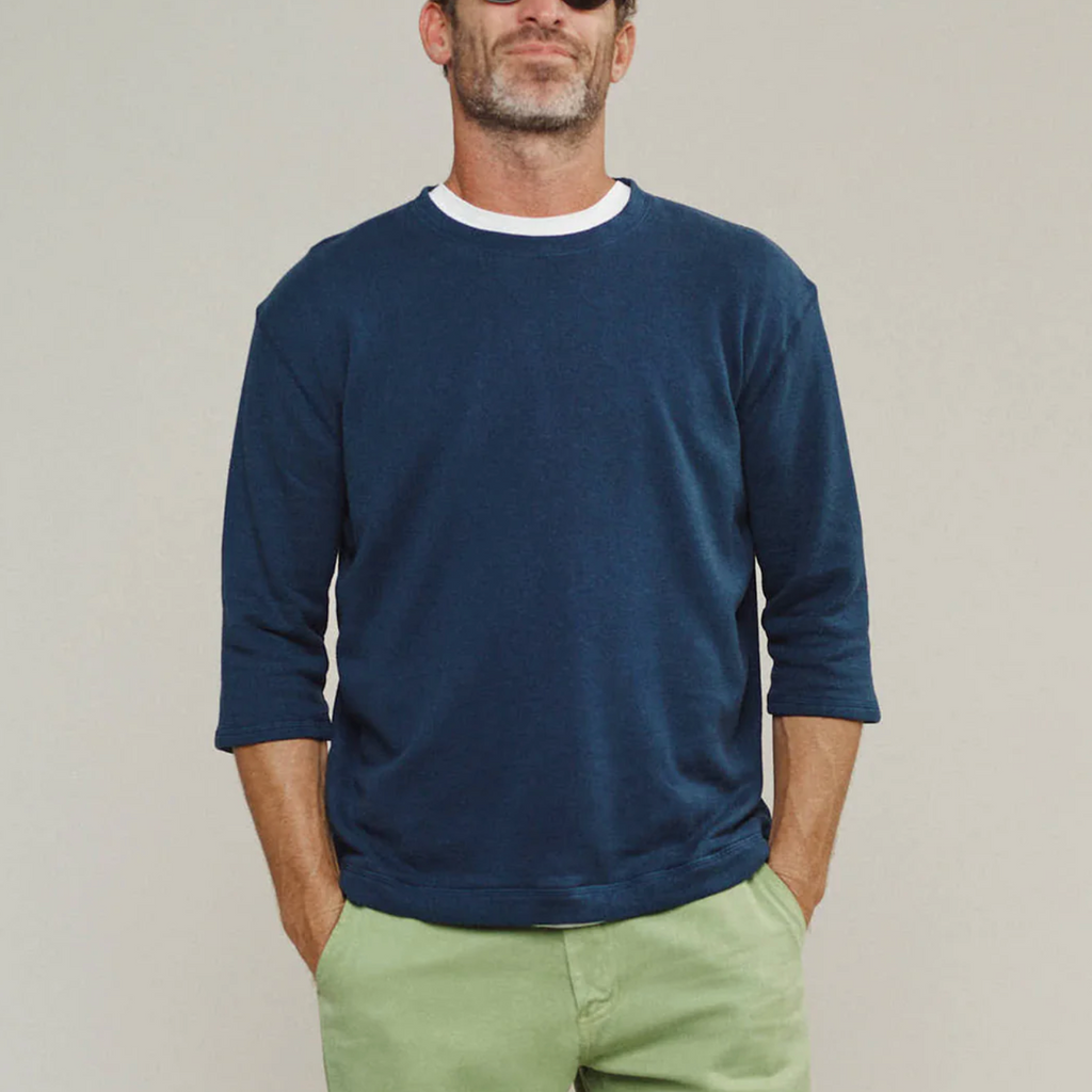 Man wearing a navy sweater and light green pants against a plain background