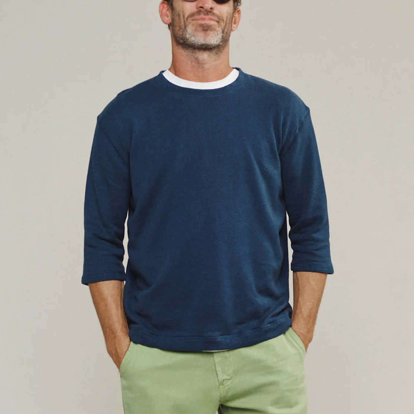Man wearing a navy sweater and light green pants against a plain background