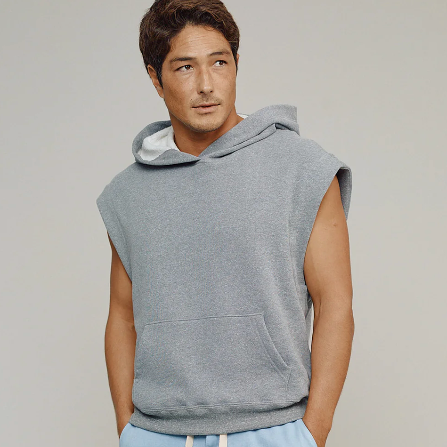 Man wearing a sleeveless gray hoodie and light blue pants against a plain background