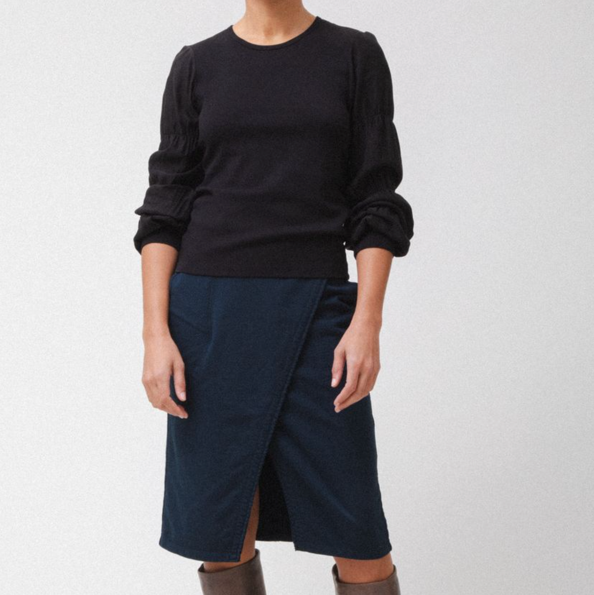 Person wearing a black sweater and navy skirt on a white background