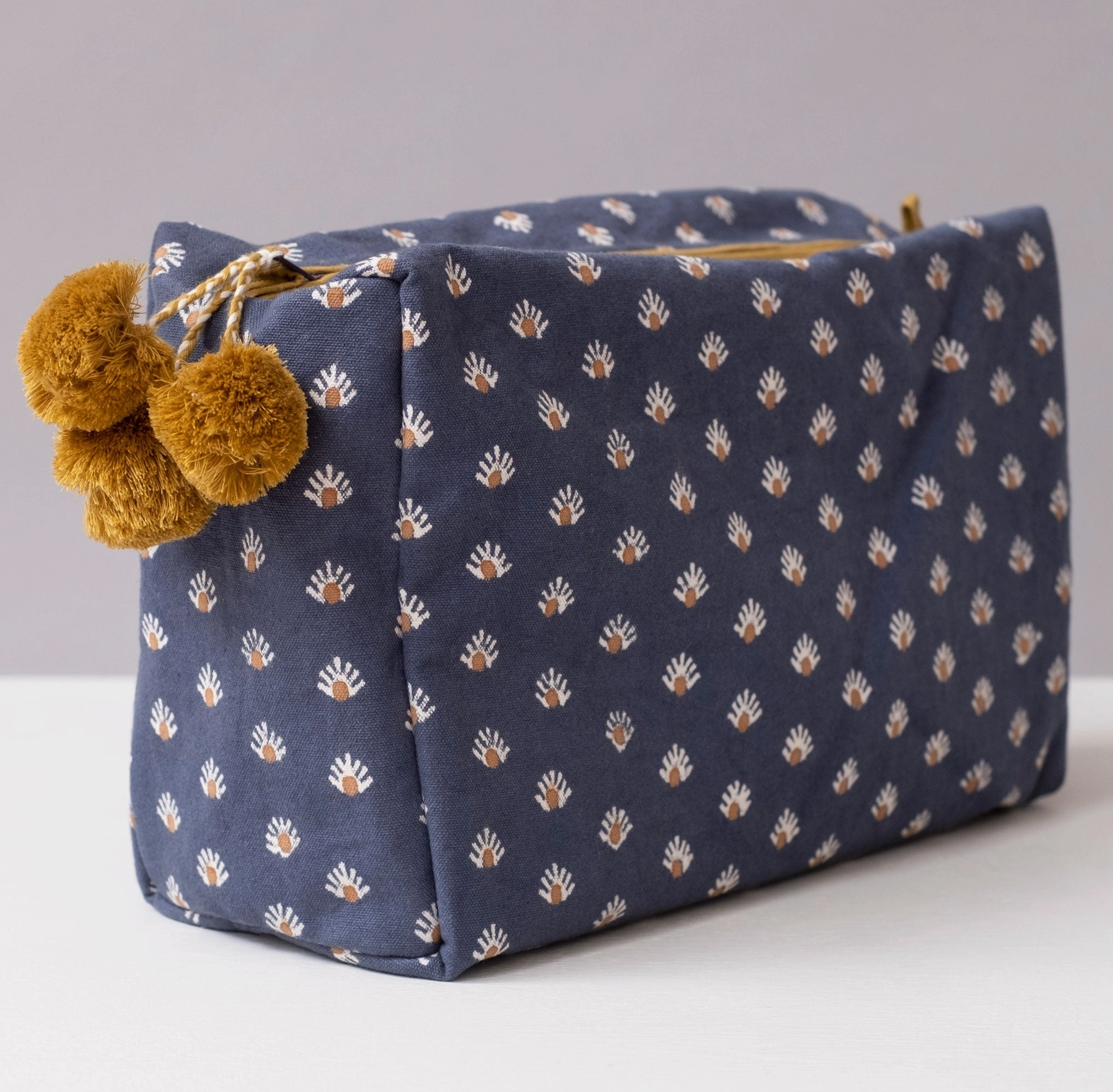 Blue patterned pouch with brown pom-poms on a light gray background