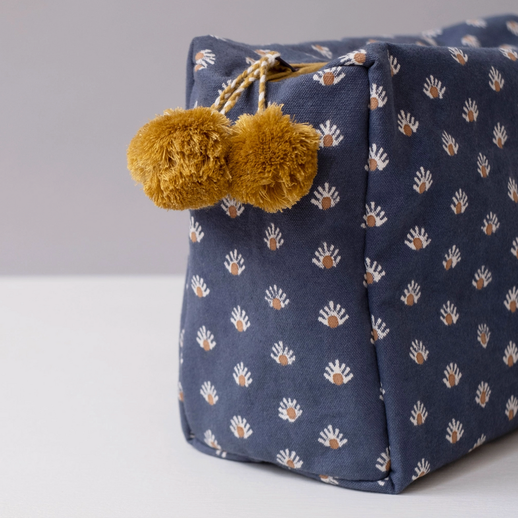 Navy blue bag with paw print pattern and gold pom-poms on a light gray background