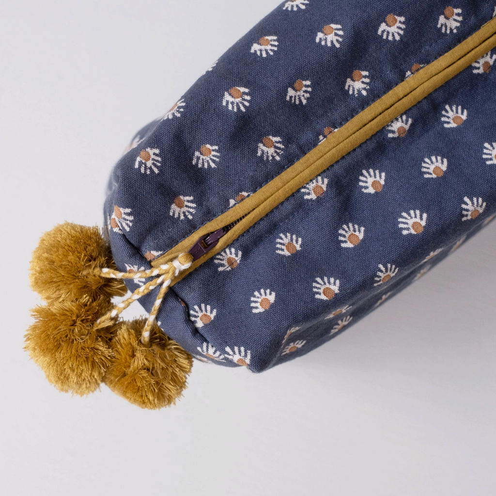 Blue pouch with white paw prints and gold zipper, accompanied by gold pom-poms on a light gray background