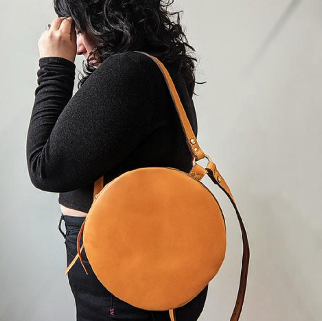 Person wearing a tan round leather bag against a plain background