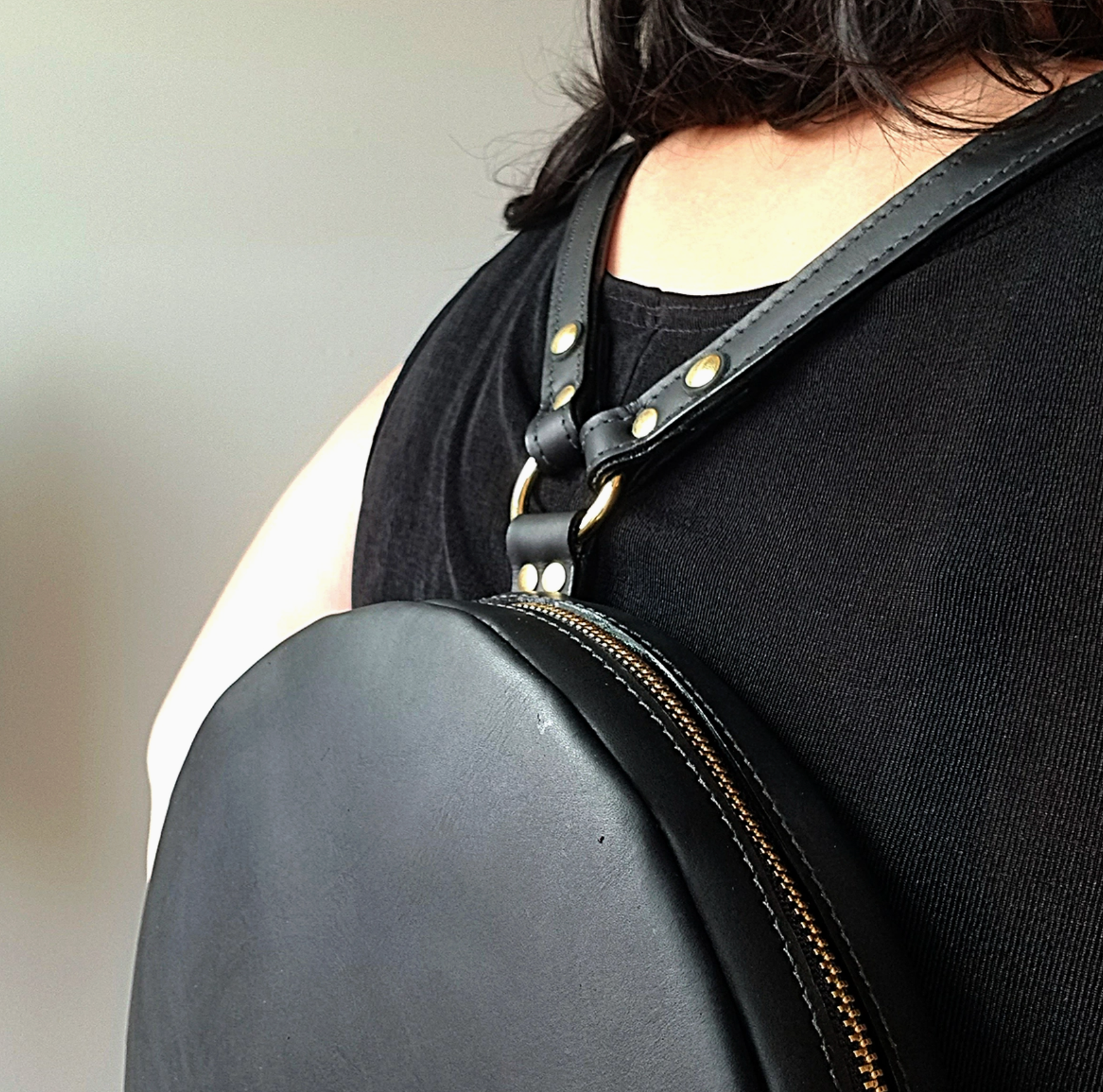 Person wearing a black leather backpack with a strap over the shoulder