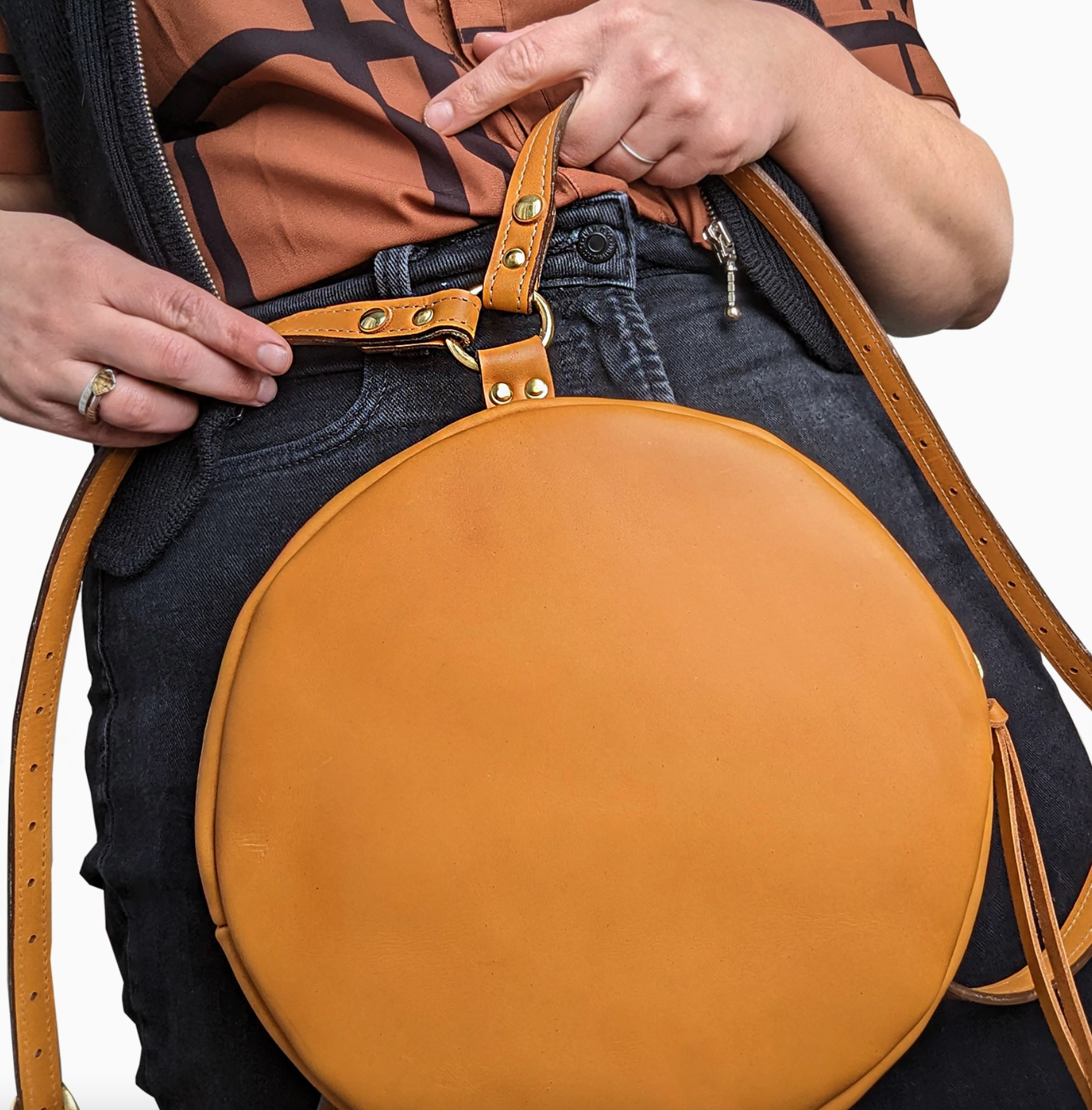 Person holding a round brown leather bag with a strap.