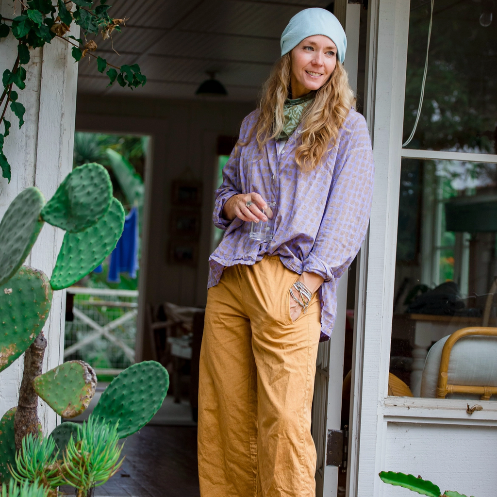 Woman standing on a wooden porch with plants and a white building in the background