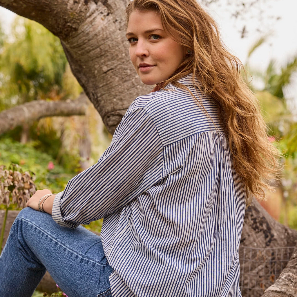 Woman sitting in a tree wearing a striped shirt and jeans.