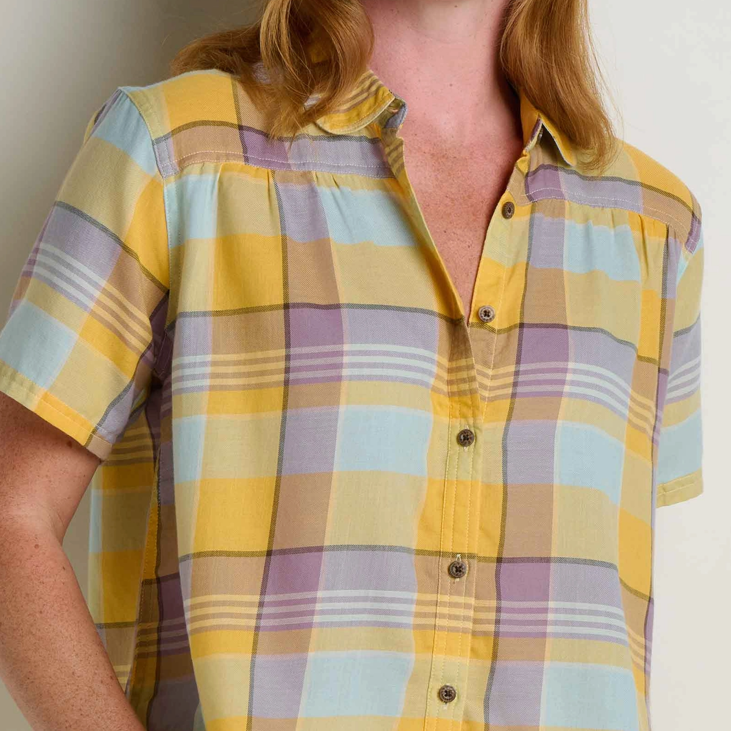 Woman wearing a yellow and purple plaid shirt against a plain background