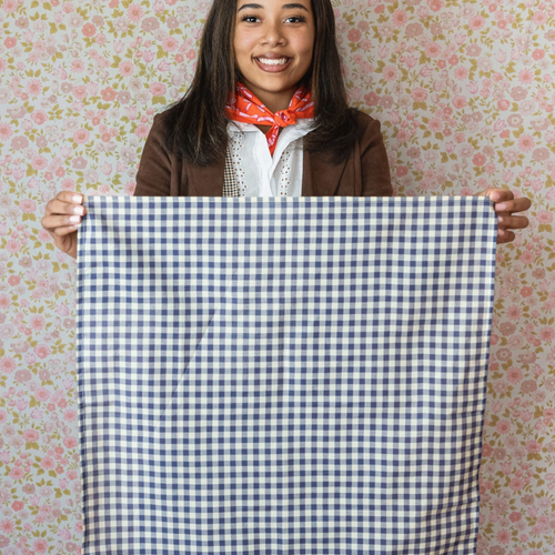 Person holding a blue and white checkered fabric against a floral wallpaper background