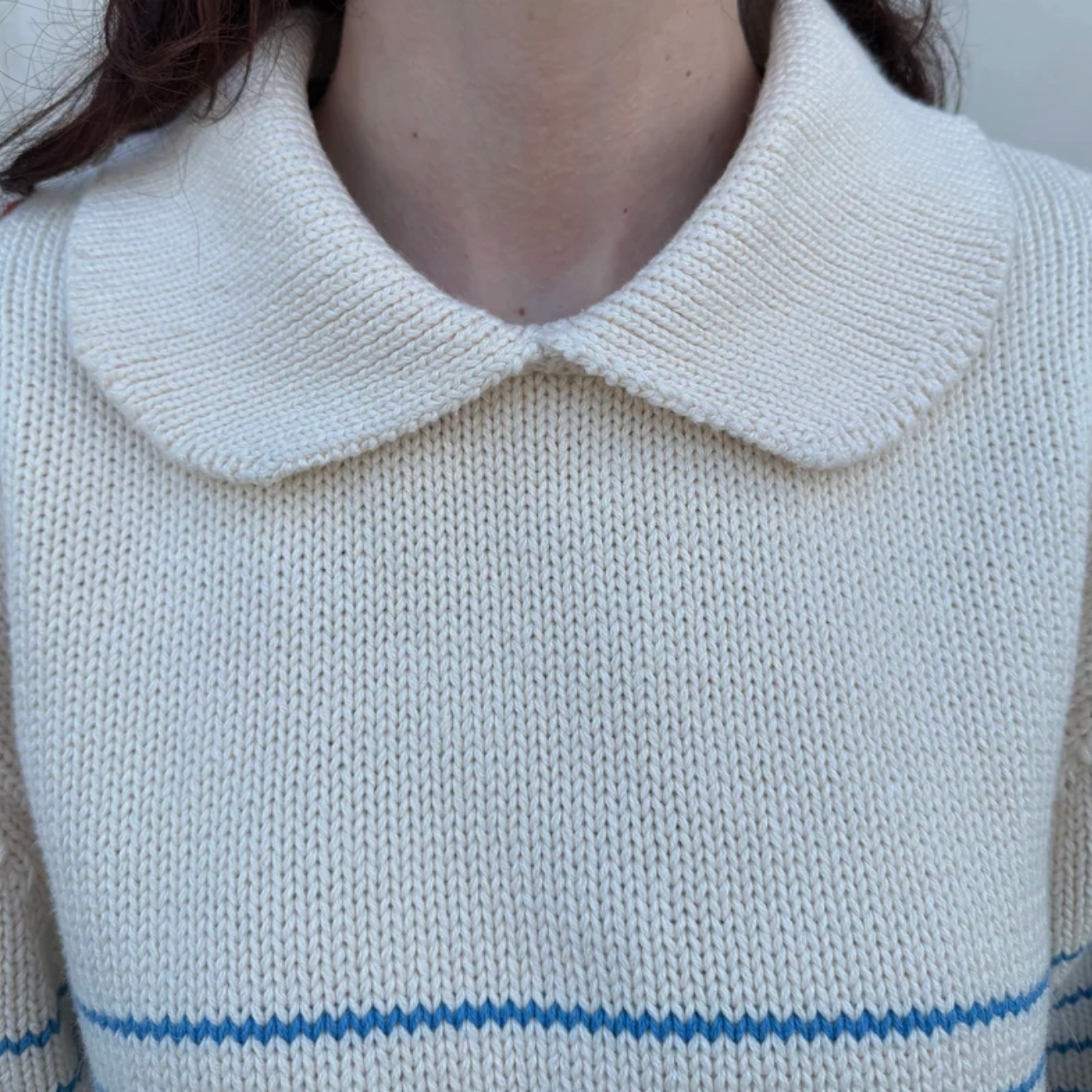 Close-up of a person wearing a white sweater with a Peter Pan collar and blue stripes.
