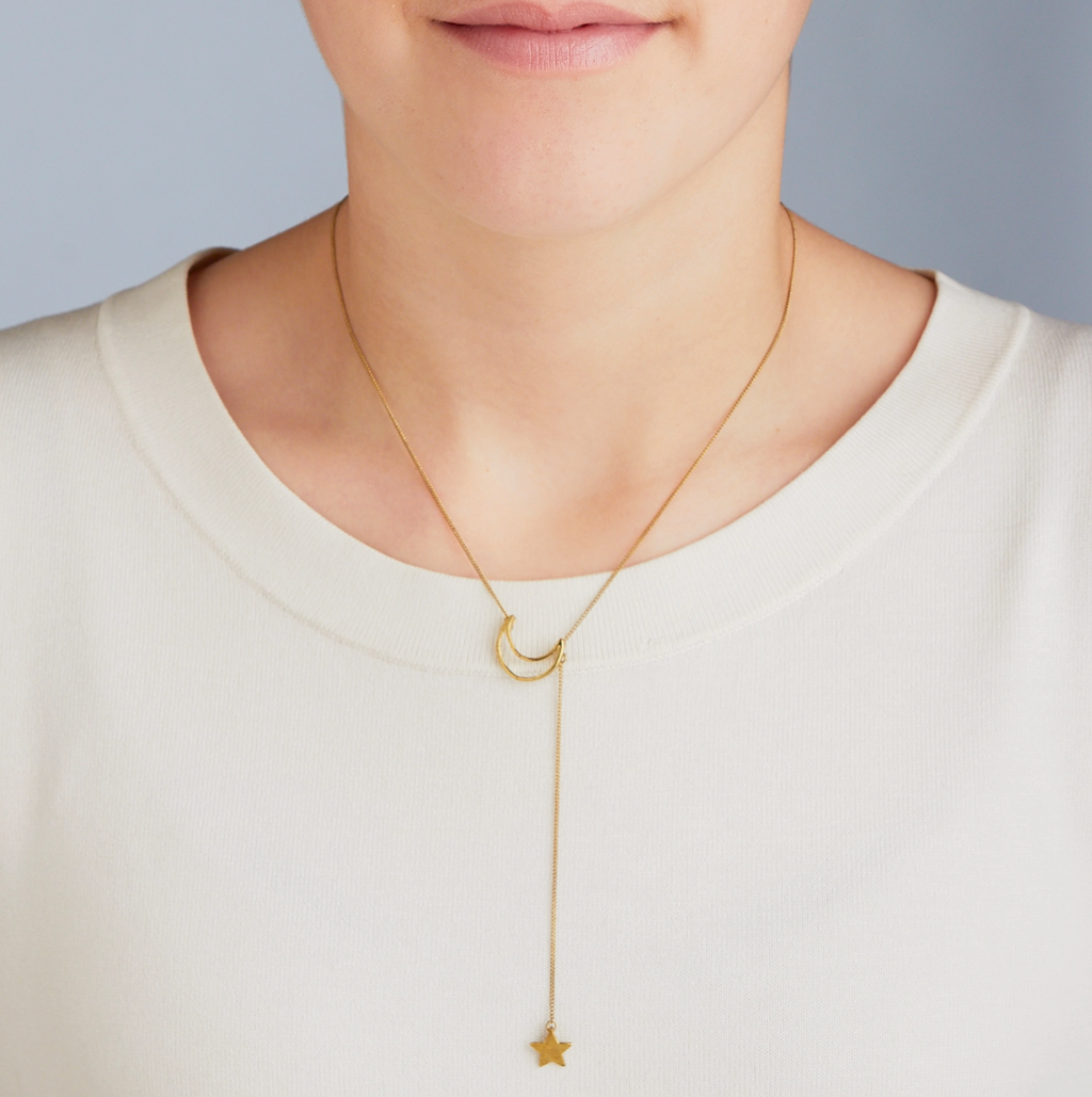 Gold necklace with star pendant worn by a person on a plain background