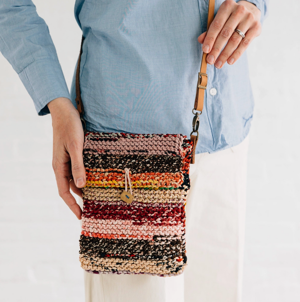 Person holding a multicolored striped crossbody bag against a white background