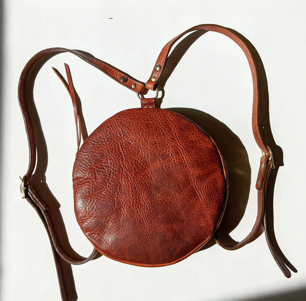 Brown leather round bag with a strap on a white background