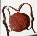 Brown leather round bag with a strap on a white background