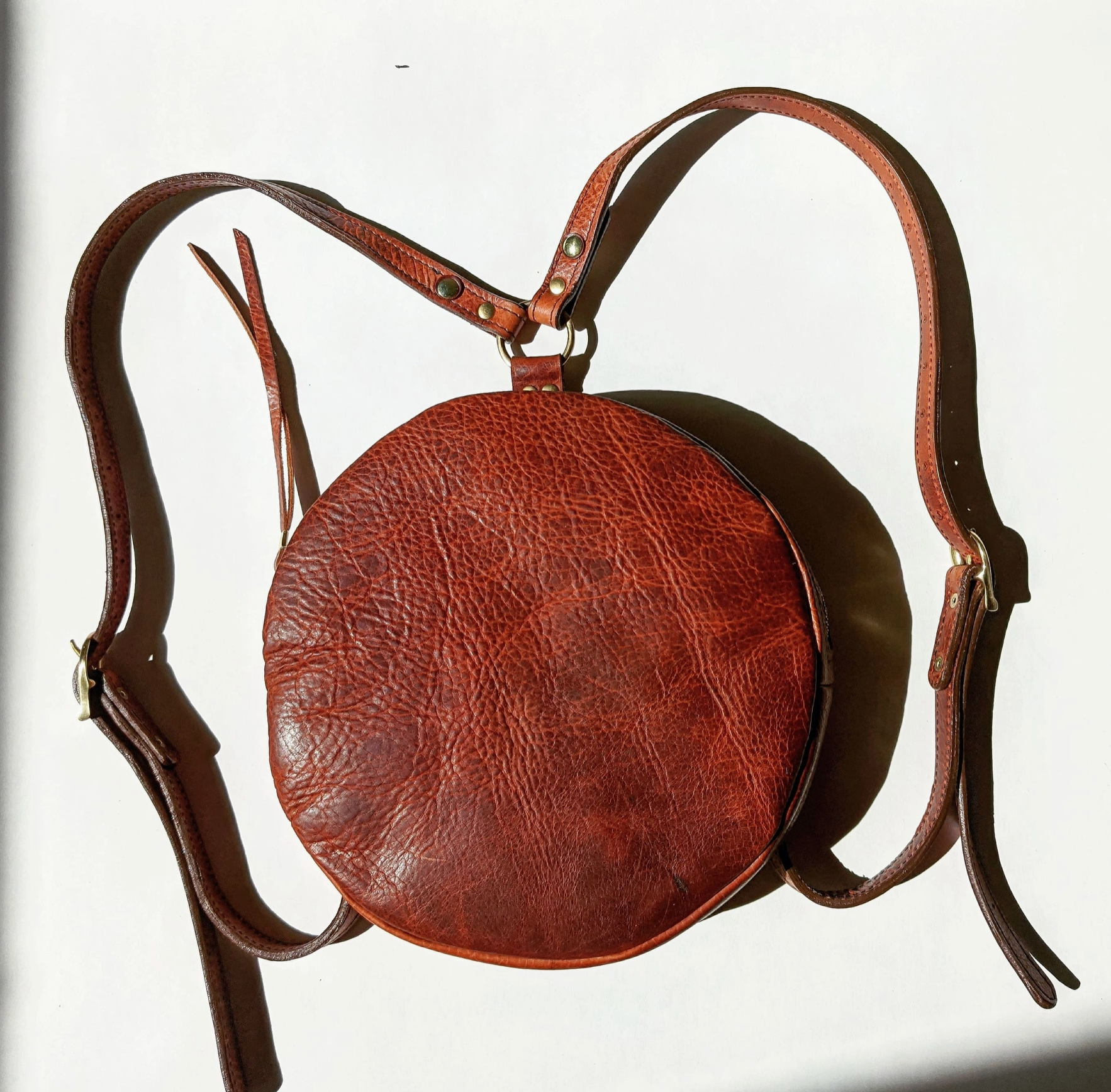 Brown leather round bag with a strap on a white background