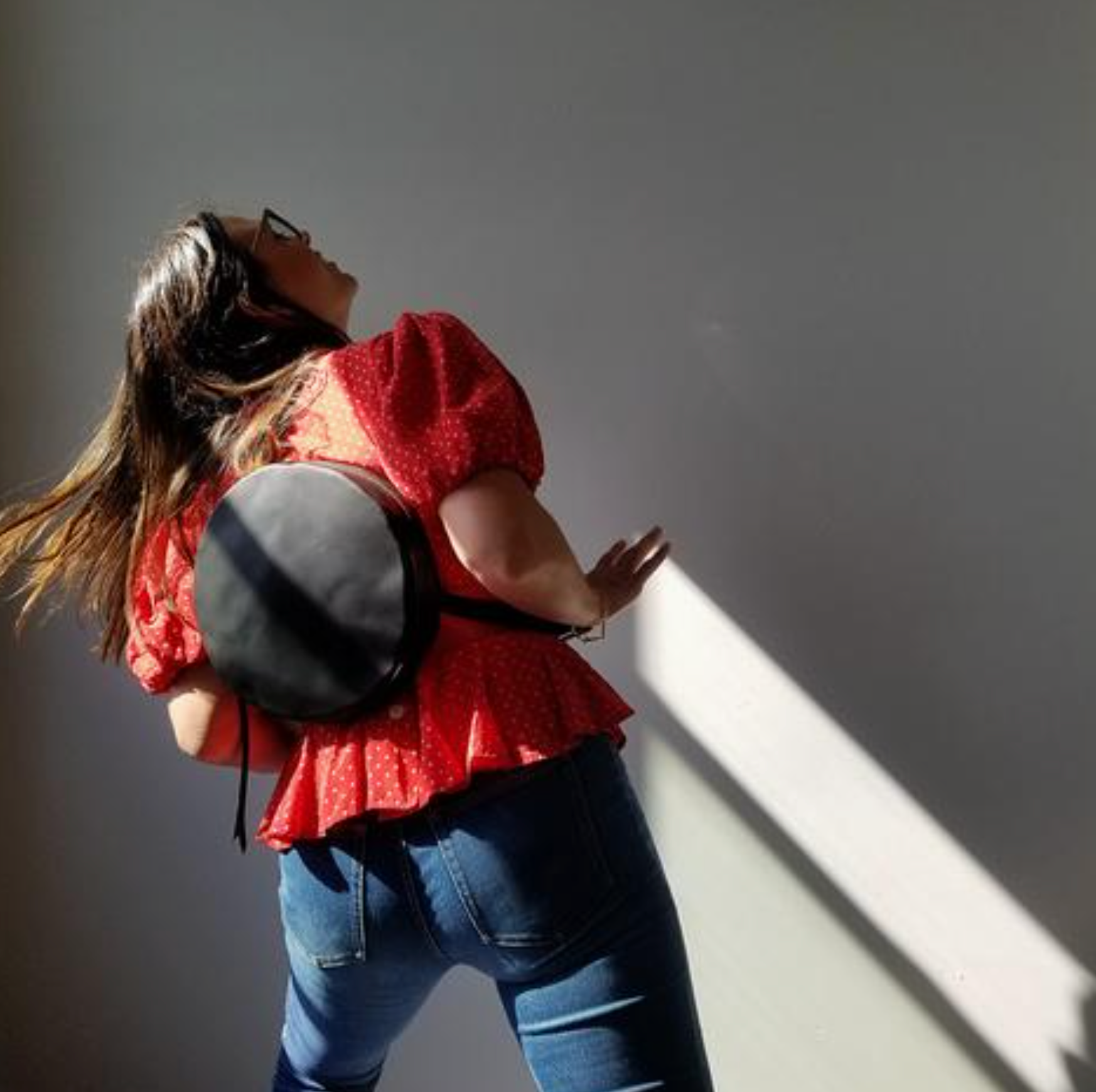 Person wearing a red top and blue jeans with a gray bag against a plain background