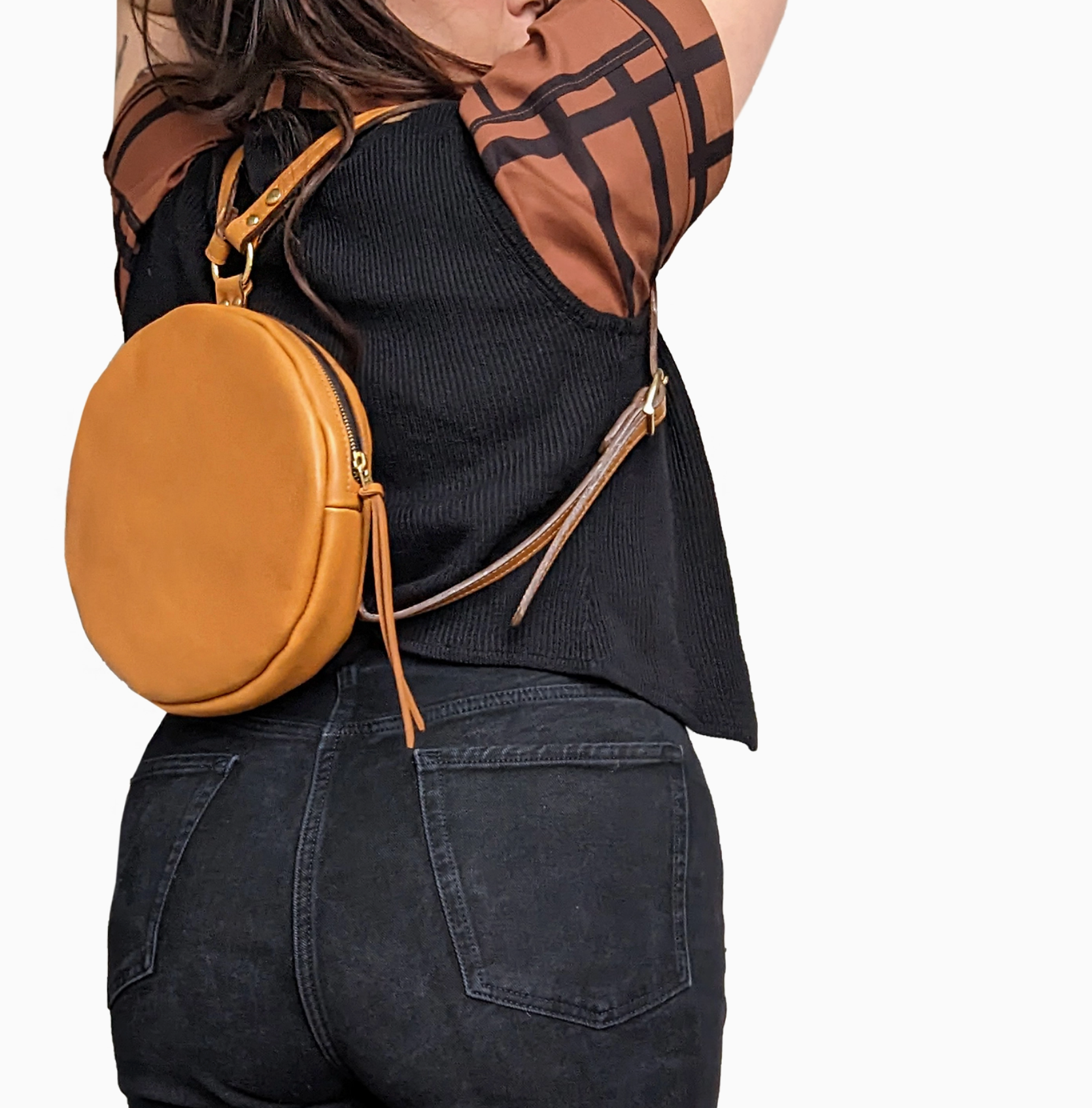 Person wearing a mustard yellow round crossbody bag with a plain background