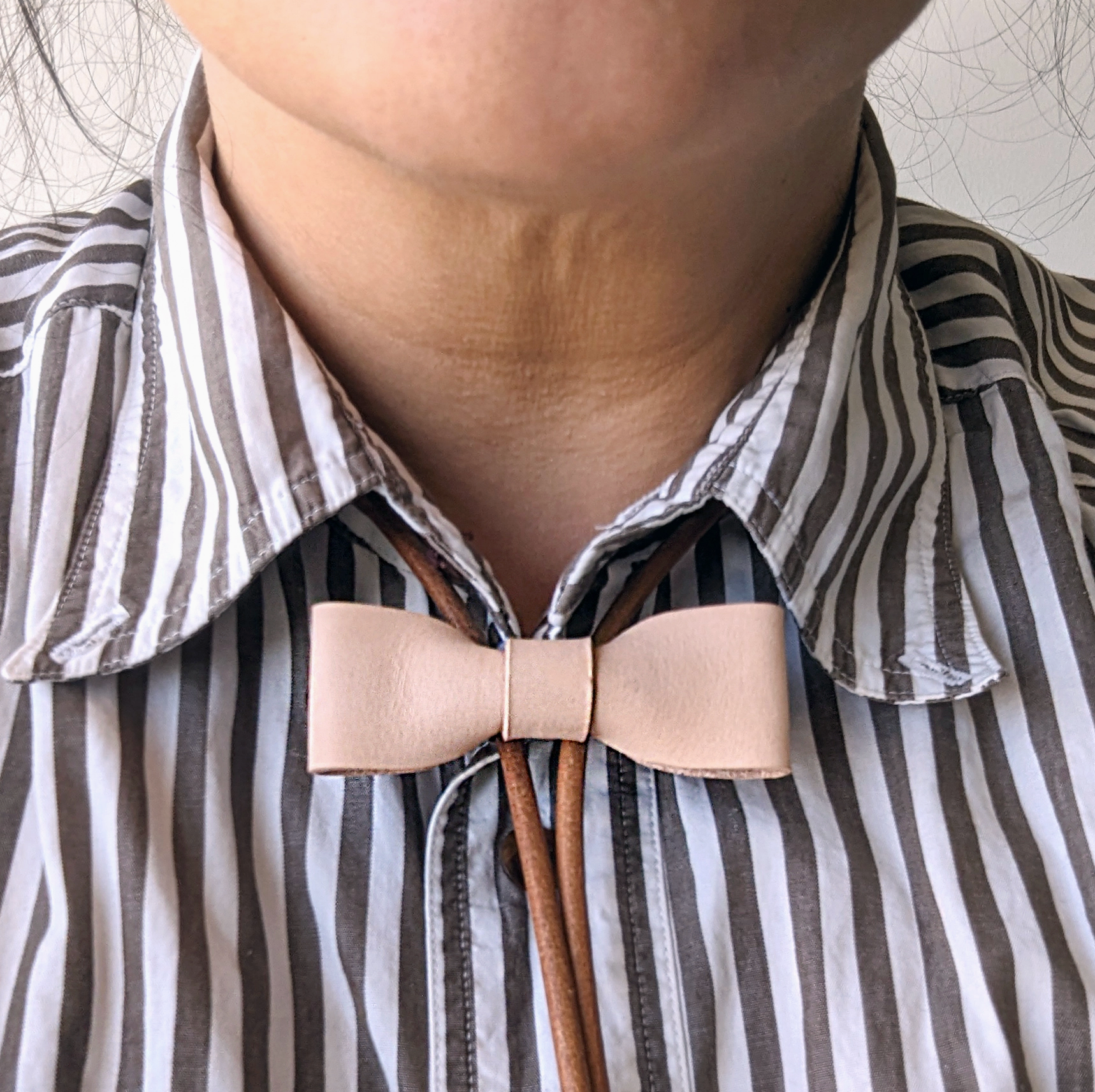 Close-up of a person wearing a striped shirt with a beige bow tie.