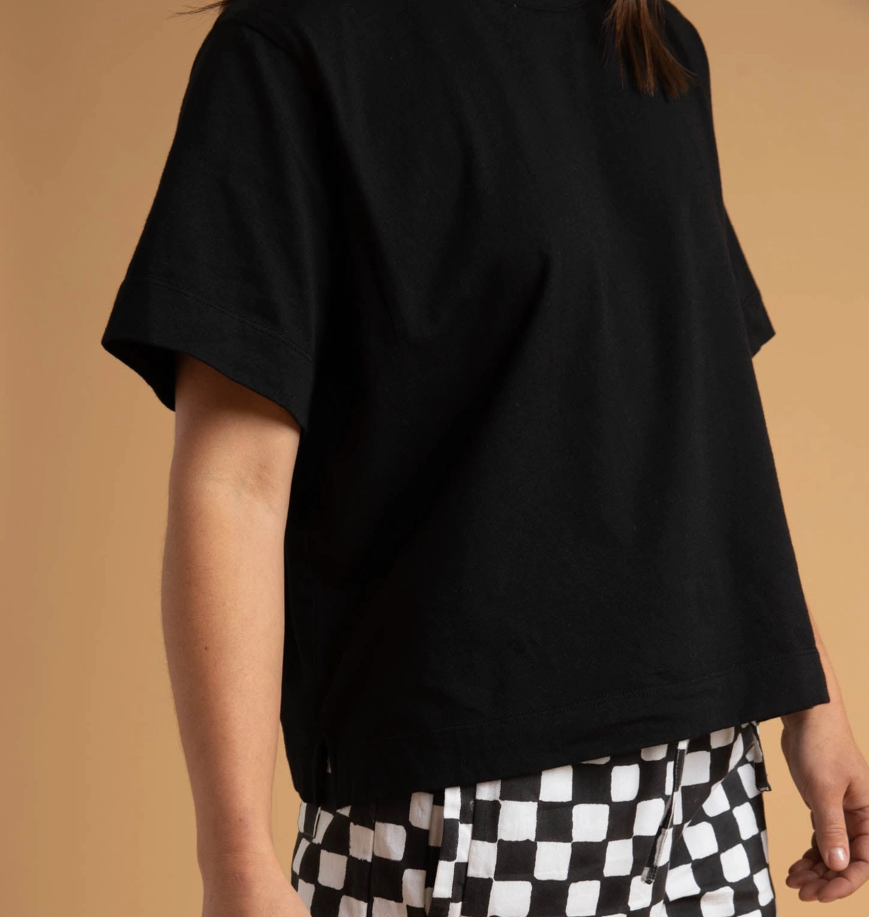Person wearing a black t-shirt and checkered pants against a beige background